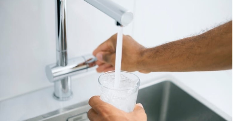 A man filling a glass with water from the kitchen faucet.