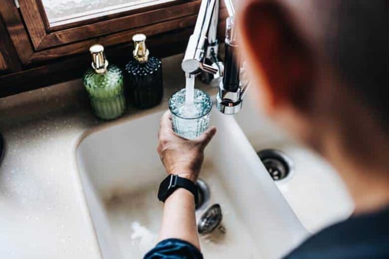 A man filling a glass with water from his kitchen sink.